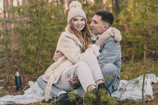 couple on a picnic in a pine forest, a girl sits in a guy's arms in a pine forest - Photo, image