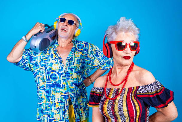 Couple of senior man and woman on holiday isolated on blue background clubbing dancing having fun holding vintage stereo - Zdjęcie, obraz