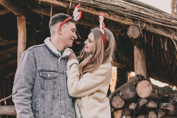 Para ubrana w noworoczne obręcze na głowach uśmiecha się do siebie na tle altanki z drewna na opał. - Zdjęcie, obraz