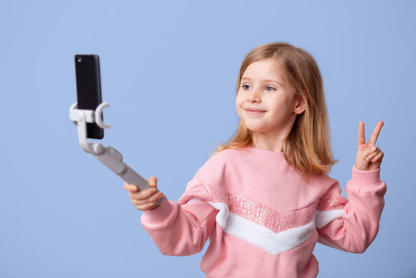 Little girl blogger influencer records videos from the blog on a smartphone, communicates with subscribers, puts likes, takes selfies,, remote learning on an isolated background. - Φωτογραφία, εικόνα