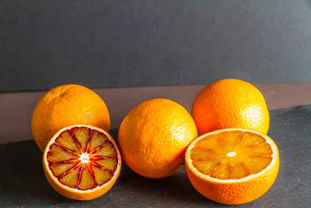 Bloed sinaasappels op een donkere achtergrond leisteen mat, een in helften, landschap, copyspace op de top, macro close-up. - Foto, afbeelding