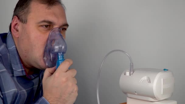 el hombre sostiene una máscara respiratoria e inhala. nebulizador y máscara de oxígeno. pulverización de un medicamento que se administra al paciente a través de una máscara o un tubo respiratorio. procedimientos médicos preventivos y tratamiento - Metraje, vídeo