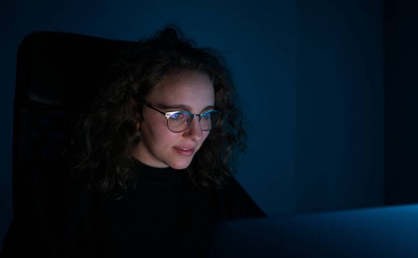 Egy nő, aki a számítógépével tanul éjszaka. Sötét van és kék a fény. A túlmunka fogalma. - Fotó, kép