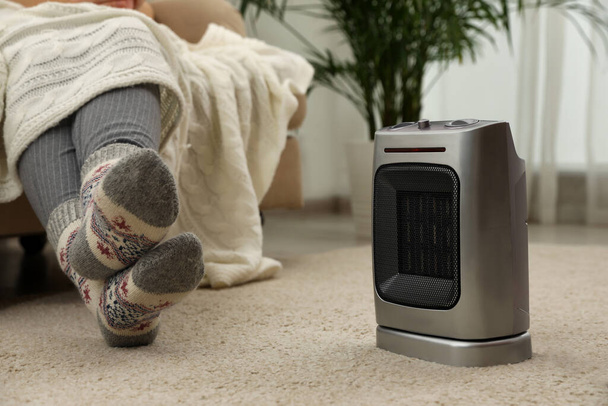 Woman warming legs near halogen heater at home, closeup - Photo, image