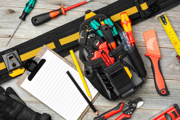 Electrician's tools on the table. An laser tape measure, screwdrivers, tongs, construction tape measure, and a level are spread out on the table. Electrician's bag with tools on the table. Top view - Photo, Image