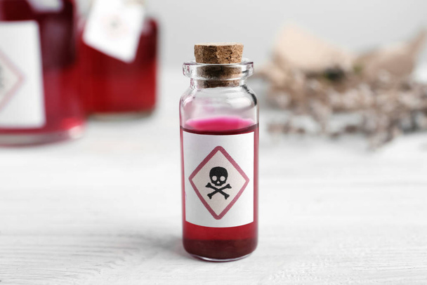 Vial of poison with warning sign on white wooden table, closeup - 写真・画像