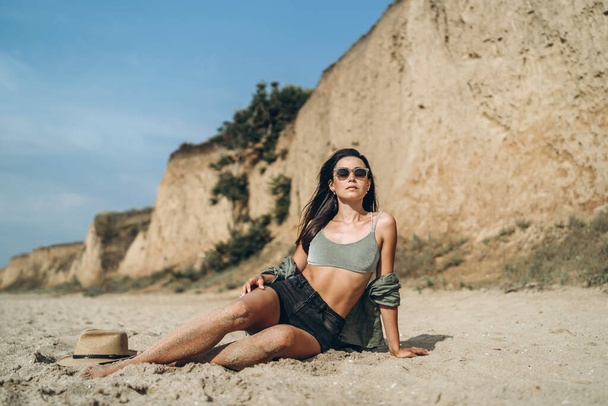 Brunette girl in hat relaxing on the beach with rocks on background - Foto, Imagem
