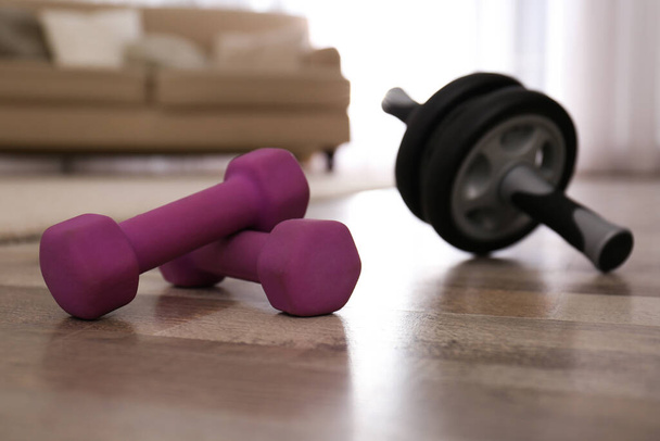 Pink dumbbells and abs roller on floor in room. Home fitness - Φωτογραφία, εικόνα