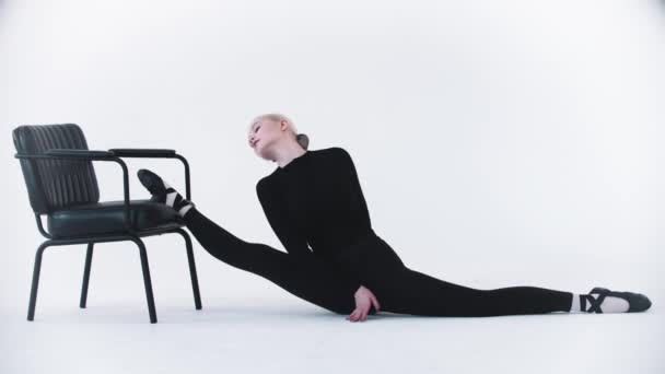 Giovane ballerina bionda che si mette la gamba sulla sedia e si allunga - Filmati, video
