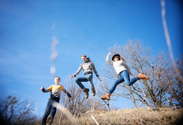 Happy cheerful smiling family jumping dancing on blue sky background in spring forest, wide angle image - Foto, Bild