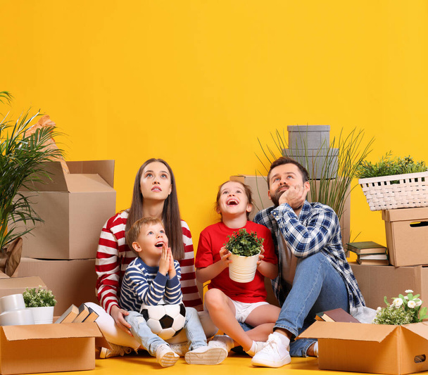 Voller Körper einer verträumten Familie: Ehepaar mit Kindern sitzt zusammen zwischen gepackten Kisten mit Habseligkeiten und stellt sich ein neues Haus vor - Foto, Bild