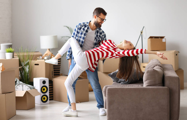 Повне тіло збудженої молодої пари розважається і танцює, насолоджуючись переїздом в нову квартиру в кімнаті з упакованими картонними коробками
 - Фото, зображення