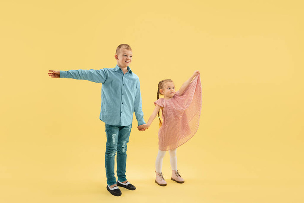Childhood and dream about big and famous future. Boy and girl isolated on yellow studio background - Фото, зображення