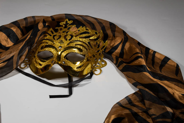 Una máscara de oro de carnaval se encuentra sobre un fondo claro. Una bufanda de seda ligera se lanza cerca.  - Foto, Imagen