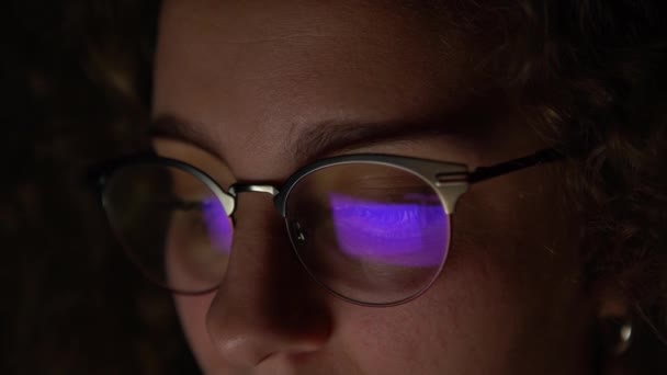 4K, Reflectie van een scherm in de bril van een vrouw die 's nachts met haar computer surft. Persoon die een computer gebruikt in het donker. - Video