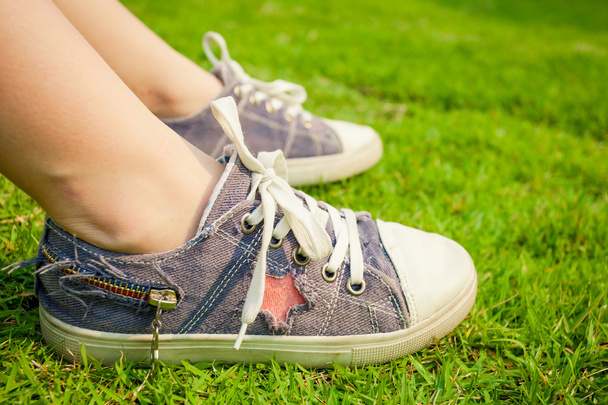 youth sneakers on girl legs on grass during sunny serene summer  - Foto, afbeelding