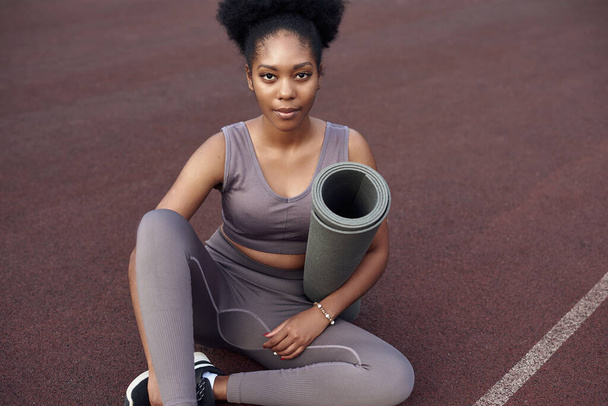 Dark-skinned beautiful girl is ready for yoga in a sports outdoor stadium. Young woman goes in for sports outdoors - Photo, Image