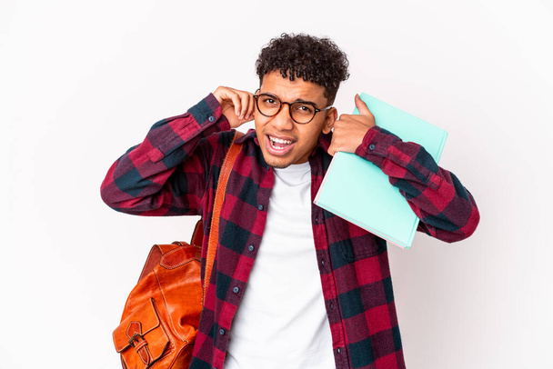 Giovane studente afroamericano riccio uomo isolato tenendo libri che coprono le orecchie con le mani. - Foto, immagini