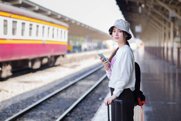 Одна азіатка носить сумку і смартфон у пошуках інформації про подорожі. Чекаючи на поїзд біля платформи. - Фото, зображення
