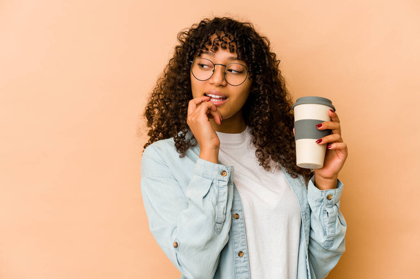 Joven afroamericana afro mujer sosteniendo un café para llevar relajado pensando en algo mirando un espacio de copia. - Foto, imagen