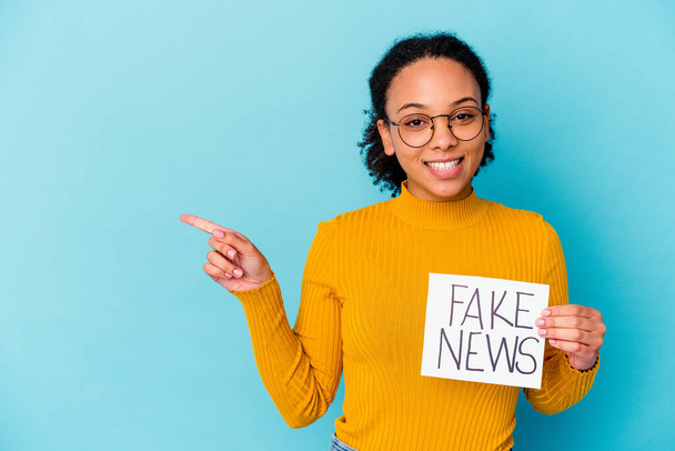 Junge afrikanisch-amerikanische Mischlingshündin mit Fake-News-Konzept, die lächelnd zur Seite zeigt und etwas im leeren Raum zeigt. - Foto, Bild
