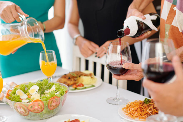 Gäste der Dinnerparty schenken Rotwein und Orangensaft in Gläser ein - Foto, Bild