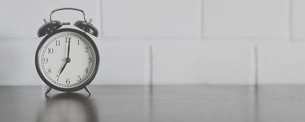 Черный винтажный будильник на коричневом деревянном столе и белом фоне цементной стены, Концепция времени. - Фото, изображение
