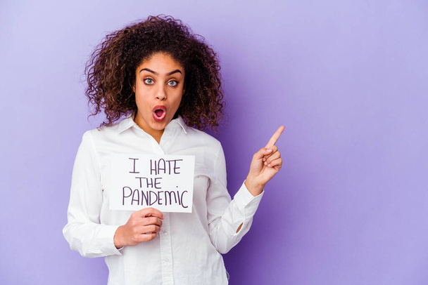 Jonge Afro-Amerikaanse vrouw houdt Ik haat pandemische plakkaat geïsoleerd op paarse achtergrond wijzend naar de zijkant - Foto, afbeelding
