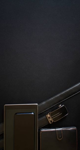 Une ceinture avec une boucle dorée, un smartphone, une tablette et un carnet reposent sur un fond noir. Observateur, programmeur ou blogueur. Élégante bannière verticale. Espace pour une inscription. Vue d'en haut - Photo, image