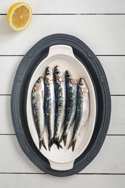Ein Foto von frischen, rohen Sardinen auf weißem Teller und weißem Holzhintergrund - Foto, Bild