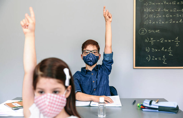 Студенты в масках поднимают руки в школе - Фото, изображение