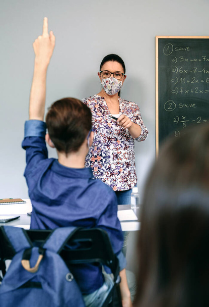 Teacher with mask in math class with student raising hand - Photo, Image