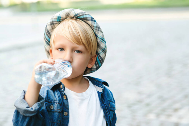 Un bel bambino che beve acqua dalla bottiglia di plastica. Bambino beve acqua all'aperto. Ragazzo che beve acqua minerale per strada. Infanzia sana. - Foto, immagini