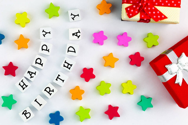 白い背景のブロックから配置されたテキスト「幸せな誕生日」、カラフルな星とギフトボックスの隣に - 写真・画像
