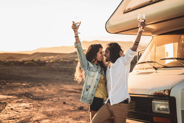 Happy beautiful hipster couple toasting with wine at sunset, standing near old camper. Travel, nomadic, real people lifestyle and emotions concept.  - Valokuva, kuva