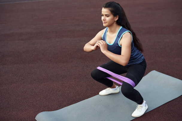 Uma linda garota balança sua coxa interna com uma faixa de fitness elástica. Esportes ao ar livre com um expansor - Foto, Imagem