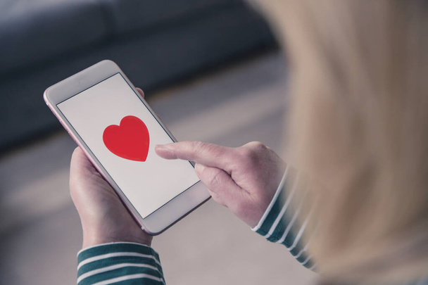 A girl tapping the touchscreen of her mobile phone to like and find love with an online dating app - Photo, Image