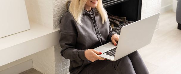 Mujer sonriente sentada navegando por Internet en una computadora portátil en casa - Foto, Imagen
