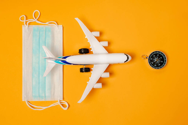 Игрушечный самолет и медицинские маски на жёлтом фоне. Концепция безопасного путешествия - Фото, изображение