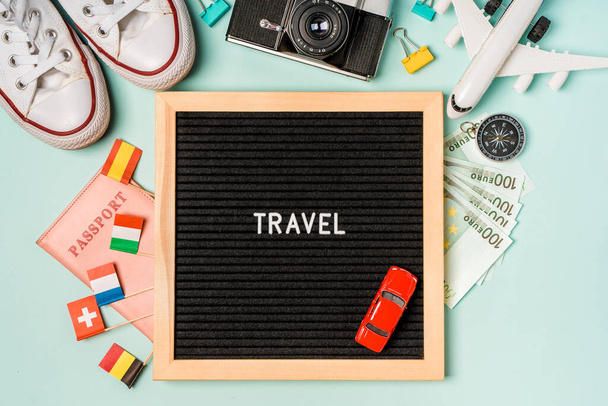  Una tabla con la inscripción "Viaje" rodeada de accesorios de viaje para el viaje: dinero, zapatillas de deporte, una cámara y banderas de diferentes países europeos. Banner para una agencia de viajes - Foto, imagen