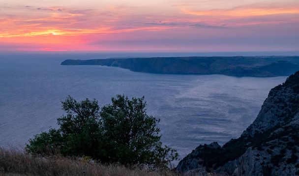 The sun setting into the sea and the long cape crashing into the Black Sea at sunset. Coast of the Crimean Peninsula near Balaklava. - Foto, afbeelding