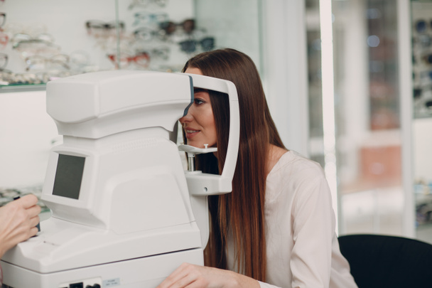 Een vrouwelijke arts en patiënt die oogheelkundige controle test met refractometer - Foto, afbeelding