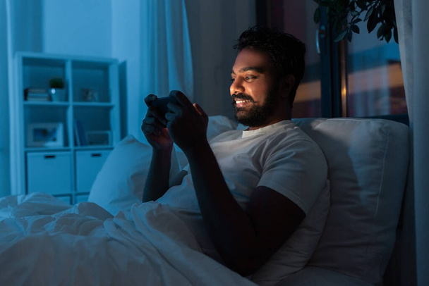 indian man with smartphone in bed at home at night - Foto, Bild