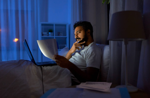 indian man with laptop and papers in bed at night - Zdjęcie, obraz