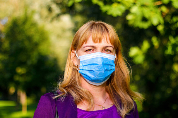 Gezicht van een blonde vrouw die een medisch masker draagt. Middeleeuwse vrouw draagt gezichtsmasker buiten in de Coronavirus Covid-19 pandemie. Selectieve focus - Foto, afbeelding