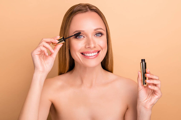 Close-up view portrait of nice attractive lovely shine cheerful glad nude naked girl applying new product brush tube mascara tone look party preparing event false effect isolated on beige background - Foto, immagini