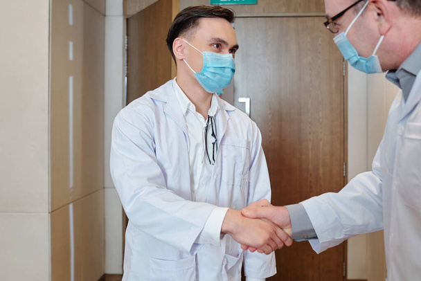 Jeune scientifique en masque médical serrant la main d'un éminent chercheur qui a inventé un nouveau vaccin - Photo, image