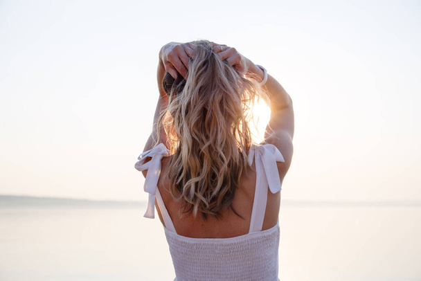 a girl with loose blonde curly hair stands with her back to the sun shining on her - Фото, изображение