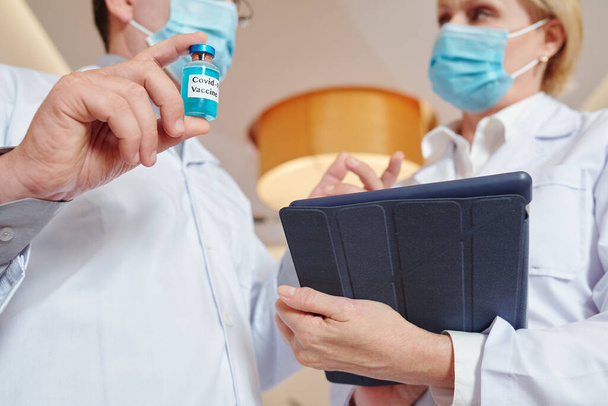 Image en gros plan d'un chercheur avec un flacon et une tablette discutant du processus d'essai d'un nouveau vaccin - Photo, image