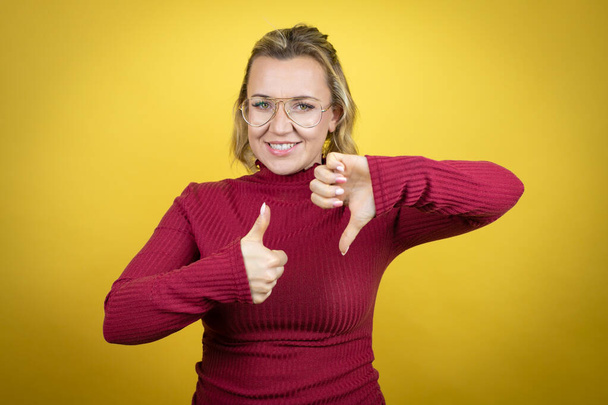 Young caucasian woman wearing casual red t-shirt over yellow background Doing thumbs up and down, disagreement and agreement expression. Crazy conflict - Fotó, kép